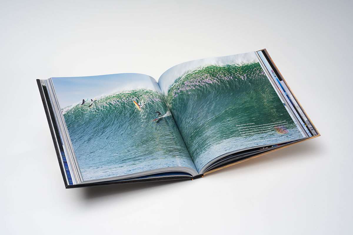 Open spread of a photography coffee table book featuring vibrant full-color big-wave surfing photographs on glossy 105lb pages