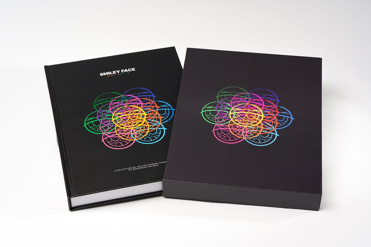 Flat-lay view of a hardcover sequential art sketchbook beside its 3.5mm hardboard slipcase with matte finish and UV coating, emphasizing 8.25x11 format