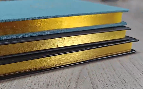 Stack of books with gold edge gilding on their pages, showcasing a shiny metallic finish.