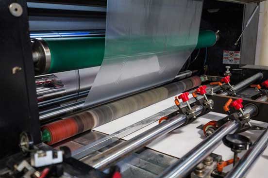 Close-up of a machine applying lamination film, with a glossy sheet being pressed onto a surface, creating a smooth, protective coating.